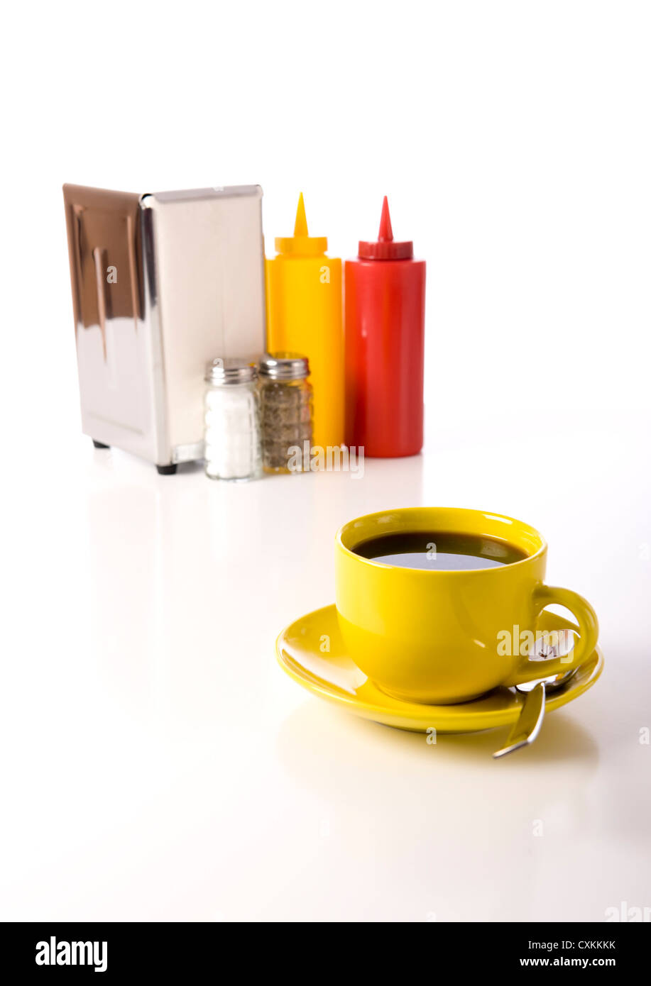 Giallo pieno tazza da caffè con il sale e il pepe shaker, Portatovaglioli e senape e ketchup su sfondo bianco Foto Stock