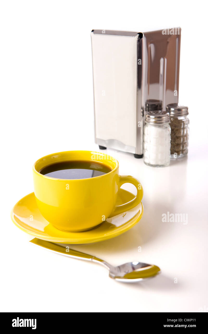 Giallo tazza di caffè con cucchiaio e una portatovaglioli e il sale e il pepe su sfondo bianco Foto Stock
