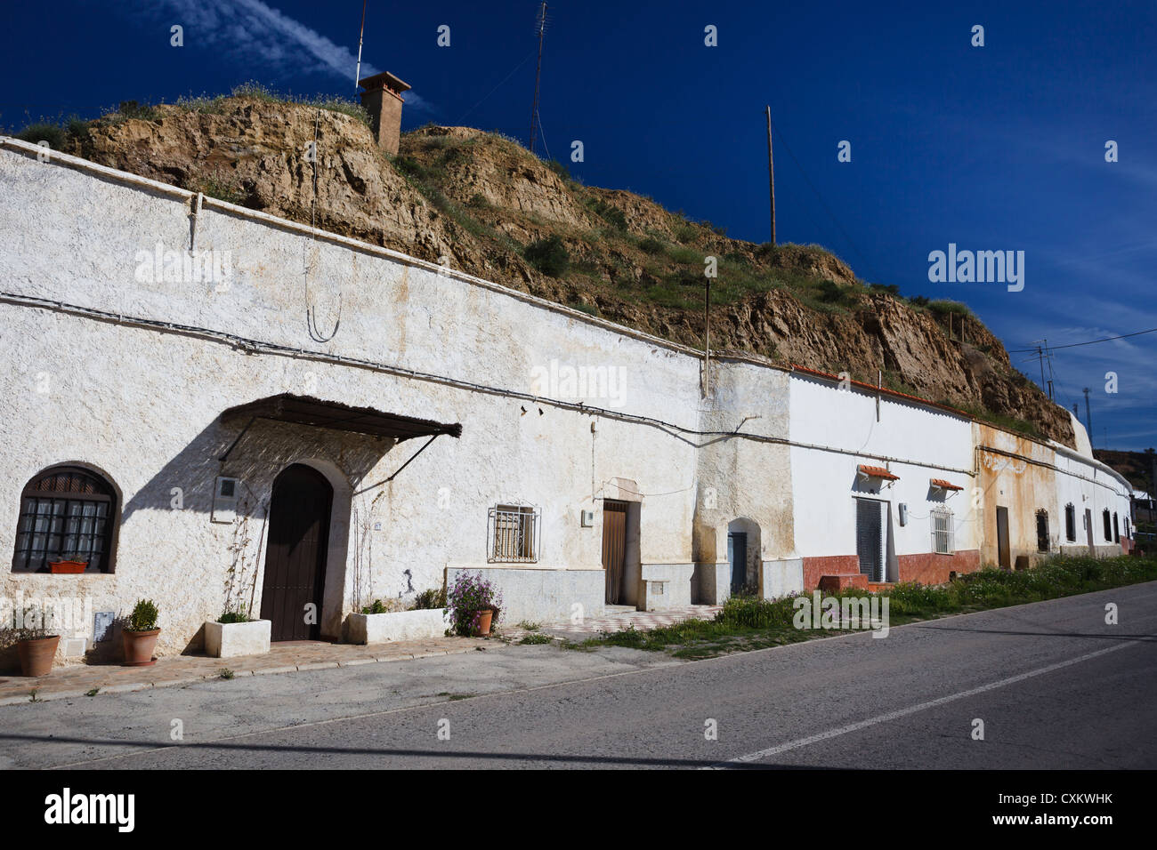 Una fila di case rupestri bianche a lato della collina fiancheggiano la strada a Guadix, in Spagna Foto Stock