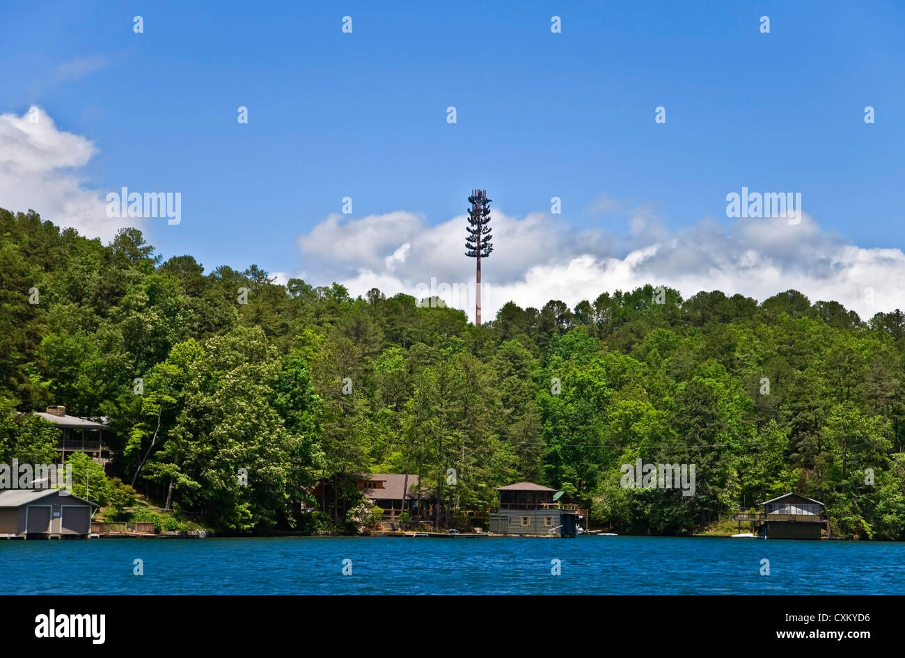 Una torre cellulare ad alta al di sopra della linea di albero in case e un lago. Foto Stock