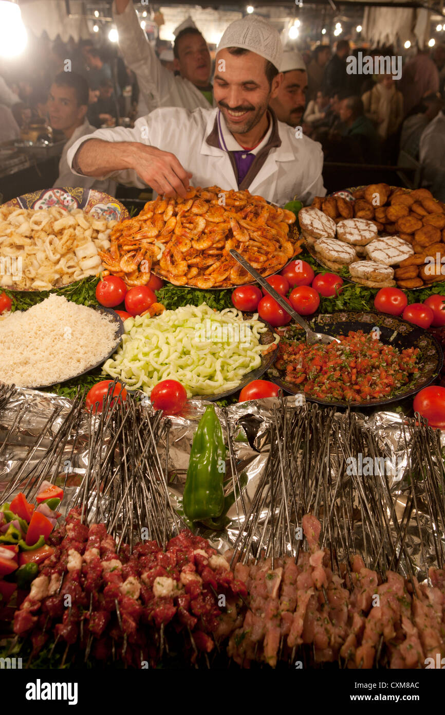 Display di cibo in stallo di mercato con cuoco locale disponendo i gamberi in Piazza Jamaa El Fna a Marrakech, Marocco Foto Stock