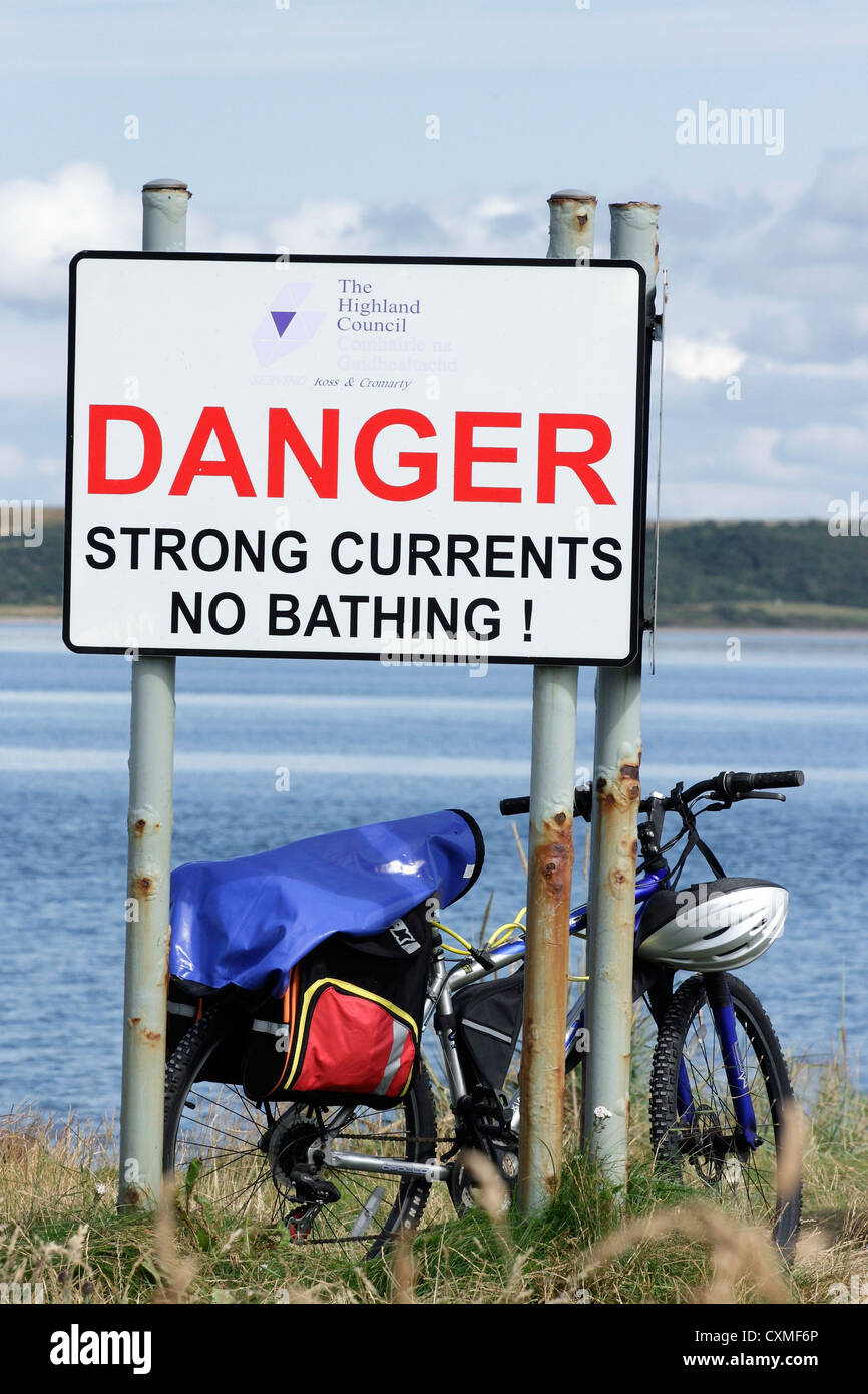 Una bicicletta appoggiata contro un segno di avvertimento di forti correnti in Moray Firth in Scozia. Foto Stock