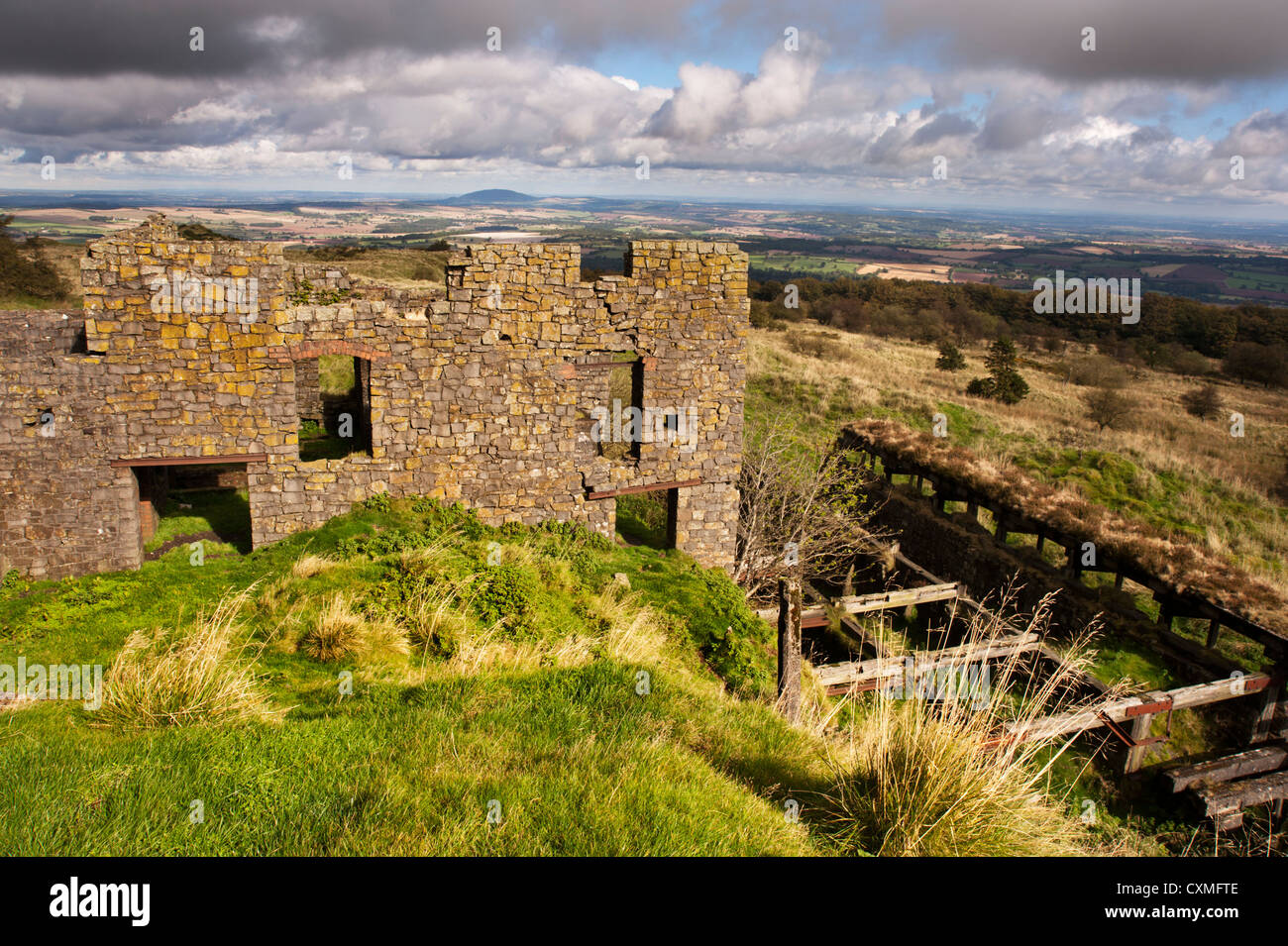 Abbandonata miniera di ex edifici sulla sommità del Brown Clee Hill, con il Wrekin hill nella distanza, Shropshire Foto Stock