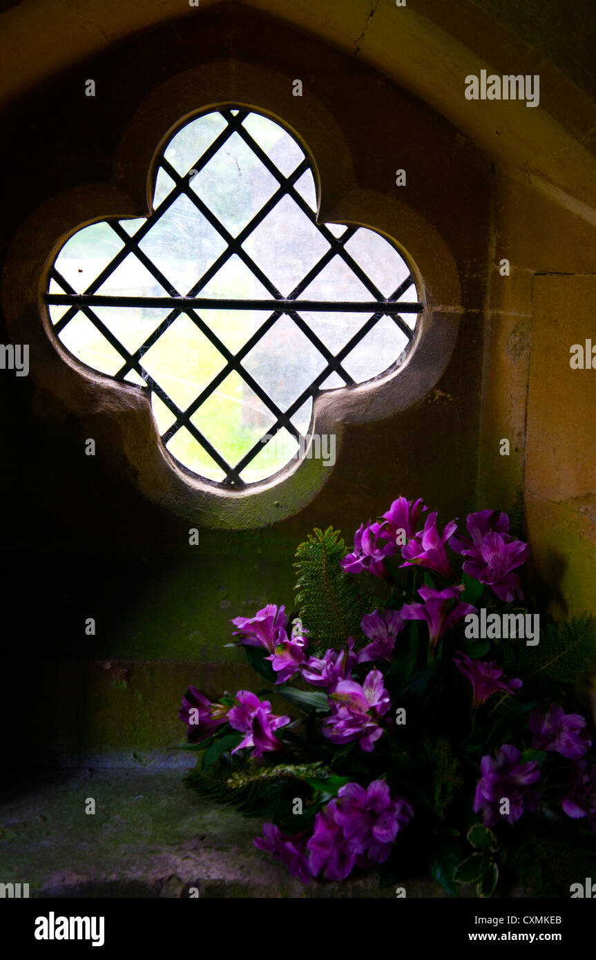 Un ornato, piombo a forma di croce nella finestra del portico di una chiesa, decorata con un bouquet di fiori viola. Foto Stock