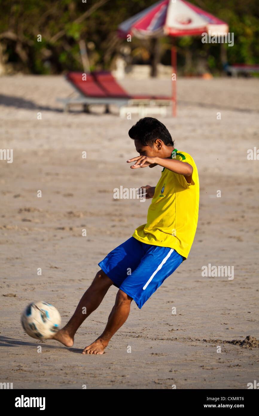 Ragazzo giocando a calcio sulla spiaggia di Kuta Beach a Bali Foto Stock