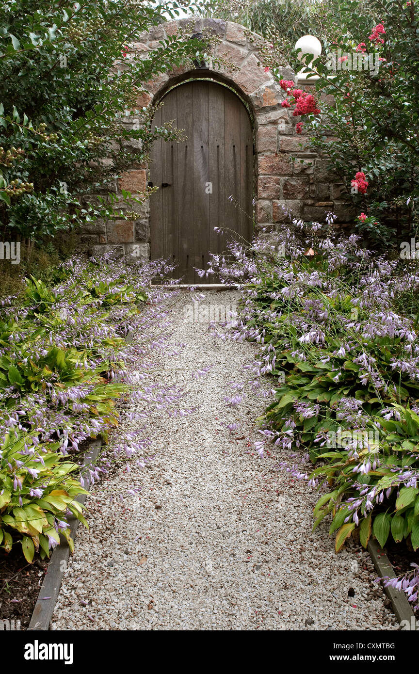 Porta di legno in giardino con fiori lungo il percorso Foto Stock