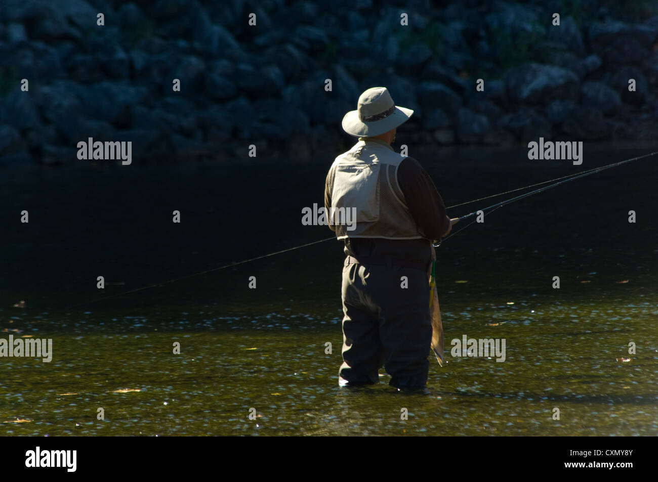 Pescatore solitario con la canna da pesca e trampolieri la pesca in un fiume sulla bella giornata di sole Foto Stock