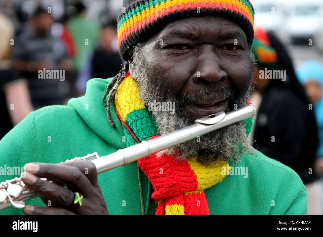 L'uomo Rastafariano suona il flauto per strada a londra vestito, in vivaci colori rastafariani indossando l'anello del dito e l'orologio da polso Foto Stock