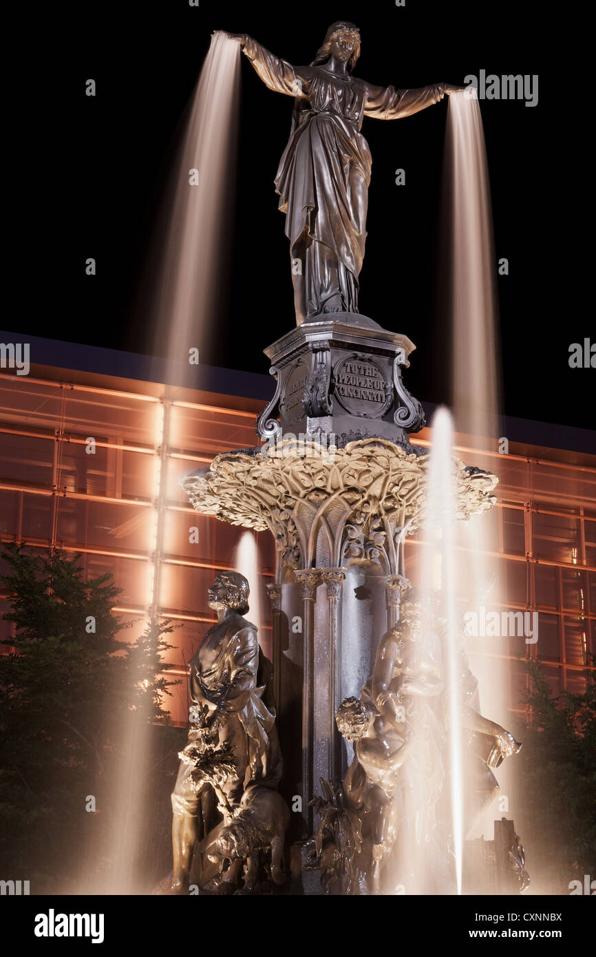 Tyler Davidson genio della fontana in Piazza Fontana, Cincinnati a notte con orange edificio illuminato Foto Stock
