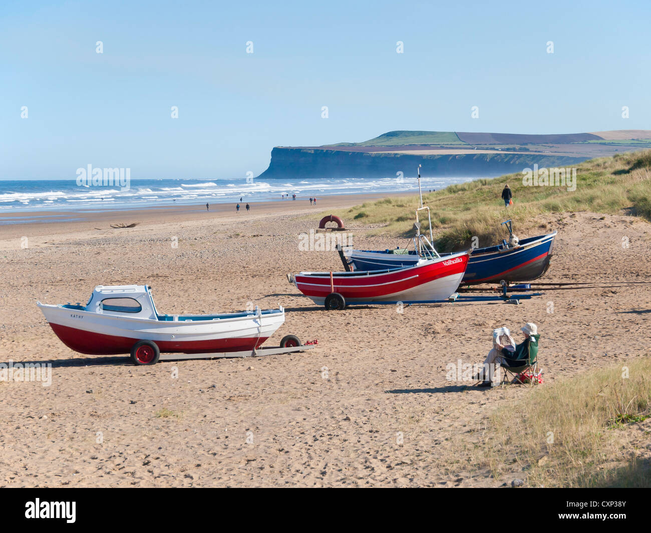 Su un soleggiato autunno domenica pomeriggio un uomo legge un giornale per le barche di pescatori sulla spiaggia di Marske Foto Stock