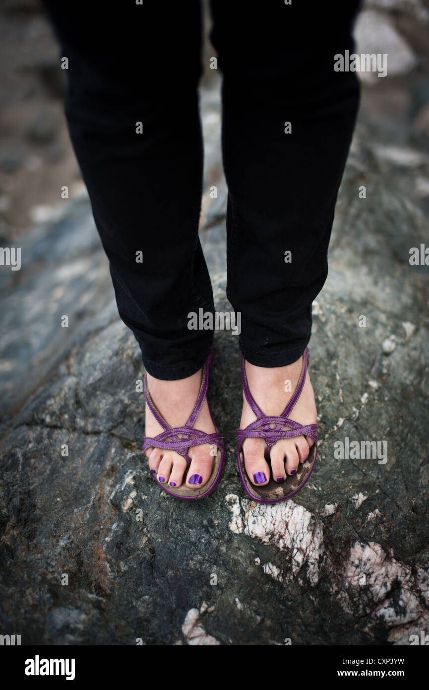 Una donna che indossa sandali viola e pantaloni neri in piedi su una grossa  pietra su una spiaggia con il mare in background Foto stock - Alamy