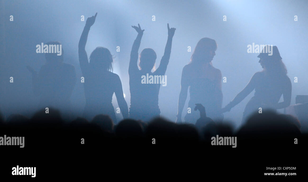 L'atmosfera durante il live concerto rock con stagliano rockers femmina ballando sul palco con le braccia in alto in aria Foto Stock