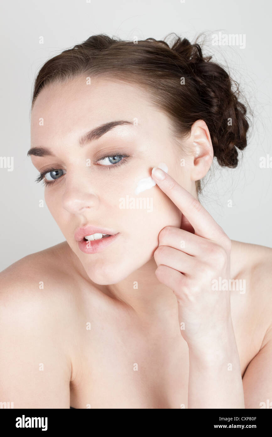 Donna che guarda in uno specchio e l'applicazione di crema per il viso Foto Stock