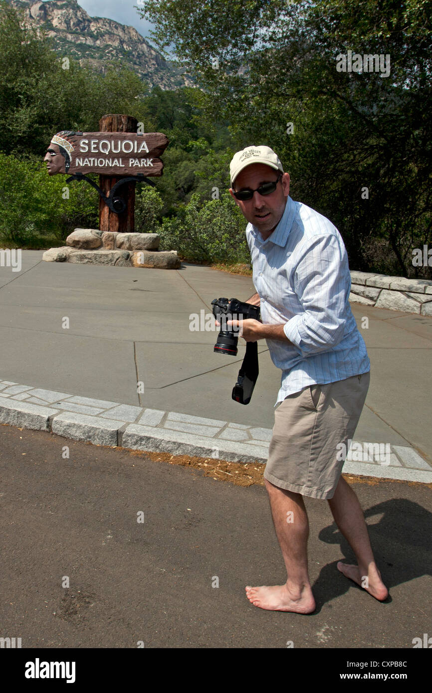 Un maschio adulto fotografo a piedi nudi in piedi di fronte entrata segno al Sequoia National Park California Stati Uniti d'America Foto Stock