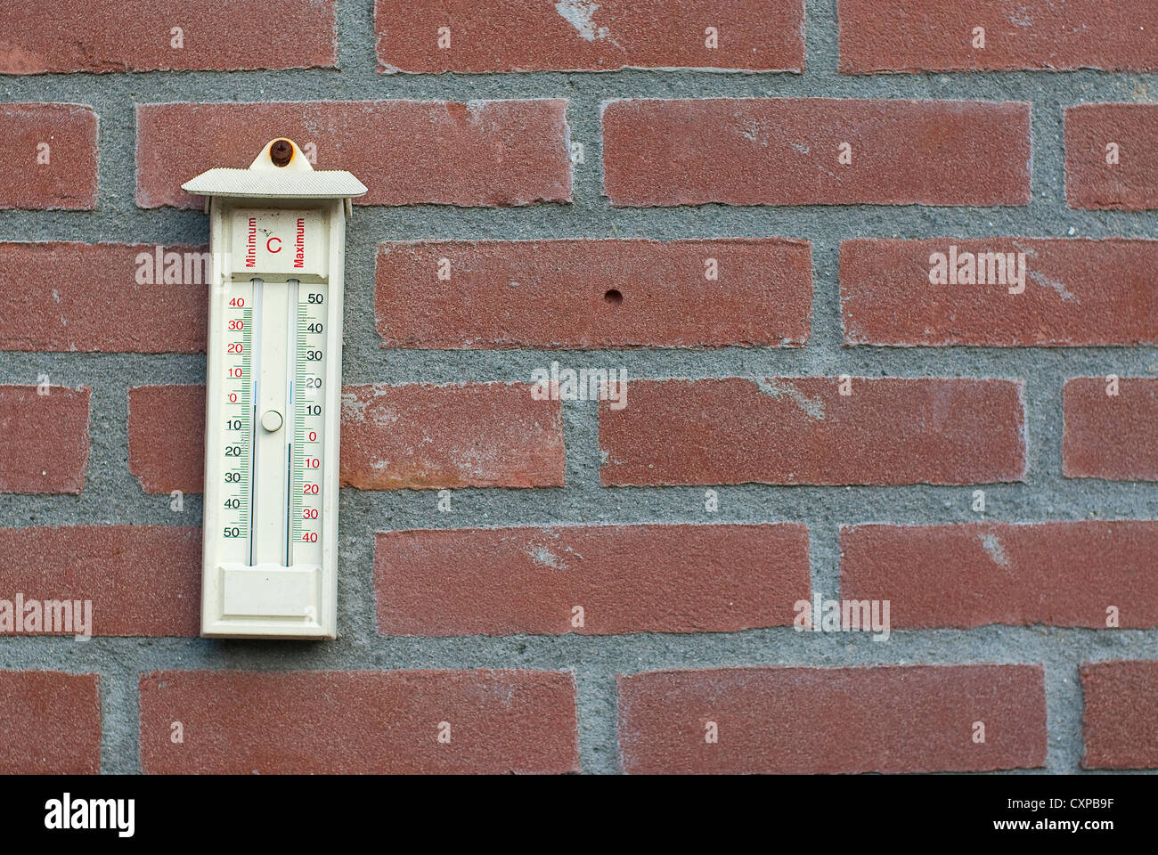 Termometro da appendere in rosso di un muro di mattoni che mostra la massima e la temperatura minima del giorno passato Foto Stock