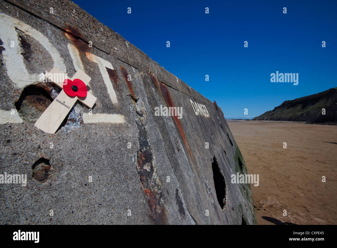 Arromanche,Normandia, Francia. Parte del "ulberry' porto artificiale dalla seconda guerra mondiale sulla spiaggia con una croce commemorativa su di esso. Foto Stock