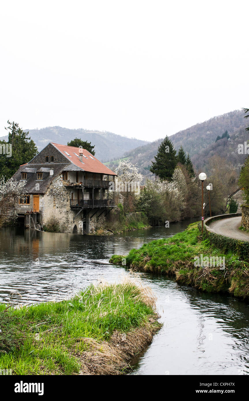 Un rustico in pietra e legno house si trova in corrispondenza del bordo di un ansa del fiume in una nebbiosa mattina nella Midi-Pirenei. Foto Stock