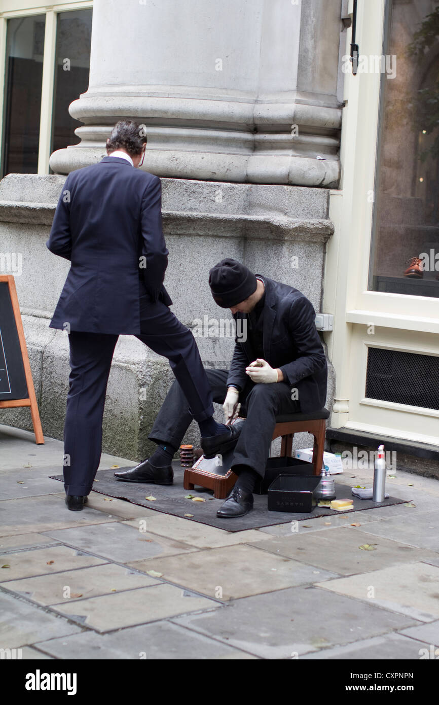 Un lavoratore della città ha le sue scarpe lucidate da un tradizionale shoeshiner nella City di Londra, nel Regno Unito, catturando un servizio di cura del corpo professionale senza tempo, la cultura aziendale e il patrimonio di scarpe brillanti nel quartiere finanziario di Londra Foto Stock