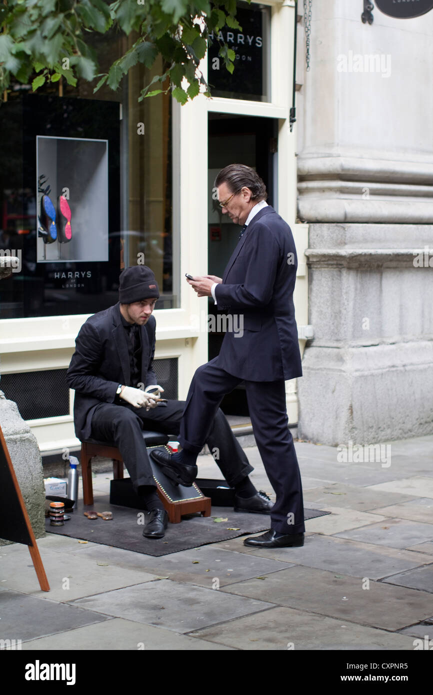 Un lavoratore della città ha le sue scarpe lucidate da un tradizionale shoeshiner nella City di Londra, nel Regno Unito, catturando un servizio di cura del corpo professionale senza tempo, la cultura aziendale e il patrimonio di scarpe brillanti nel quartiere finanziario di Londra Foto Stock