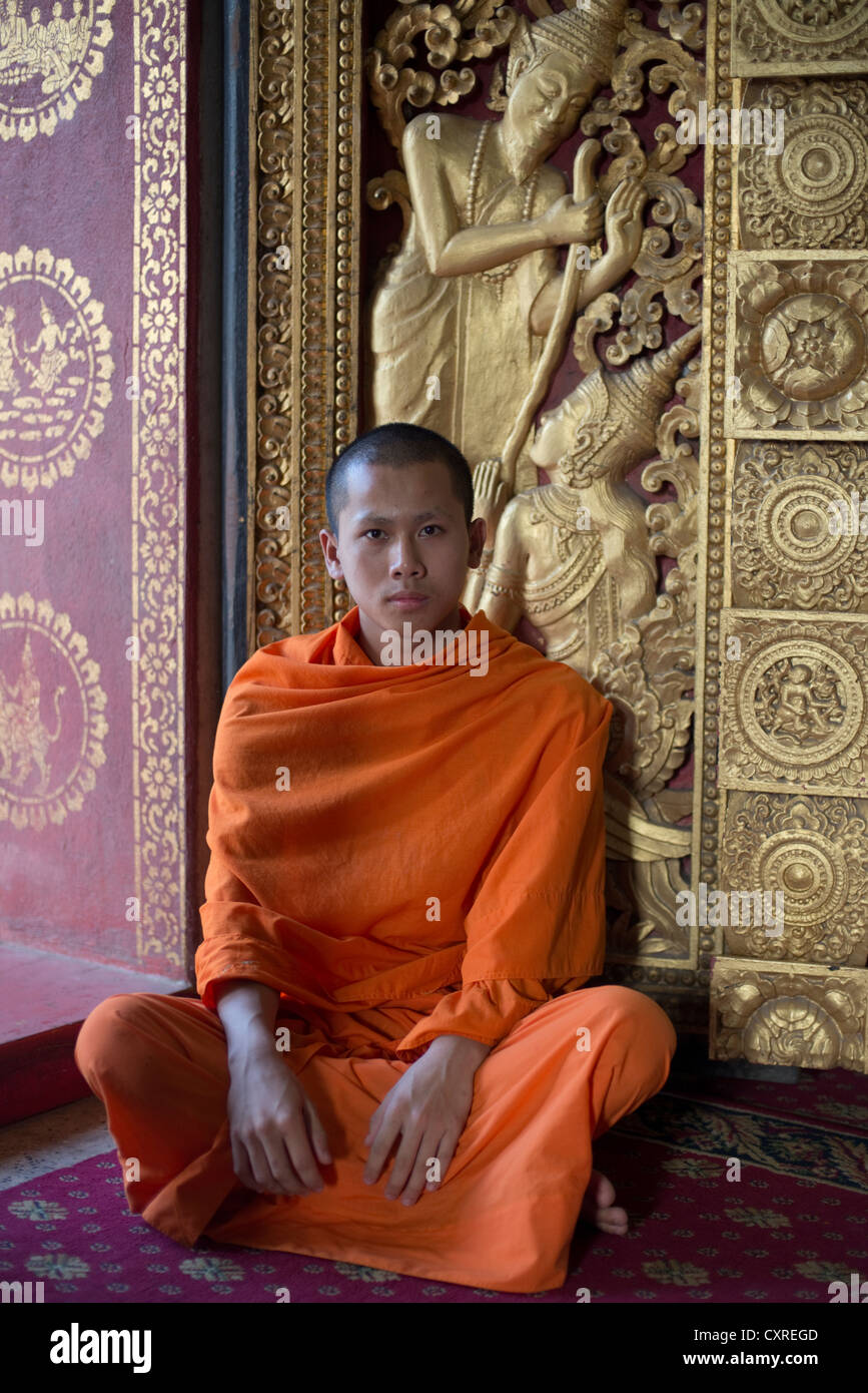 Un monaco buddista si siede nel vano della porta del suo tempio a Luang Prabang, Laos Foto Stock