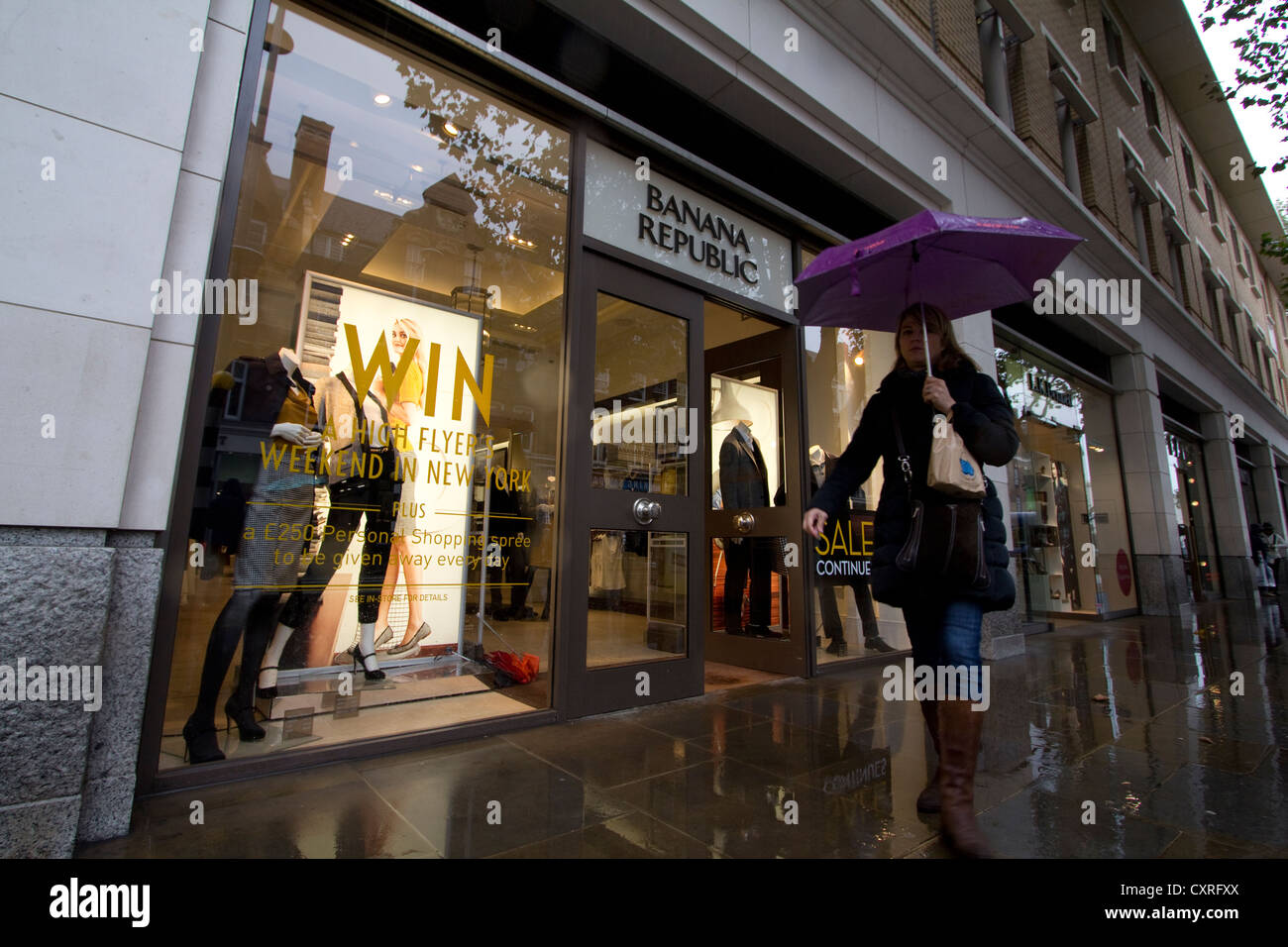 Gli amanti dello shopping con ombrelloni passano davanti all'outlet di moda Banana Republic su King's Road, Londra, Regno Unito, per catturare una giornata di pioggia in una delle strade dello shopping più iconiche della città, dove i marchi di moda globali incontrano la cultura delle strade principali britanniche Foto Stock