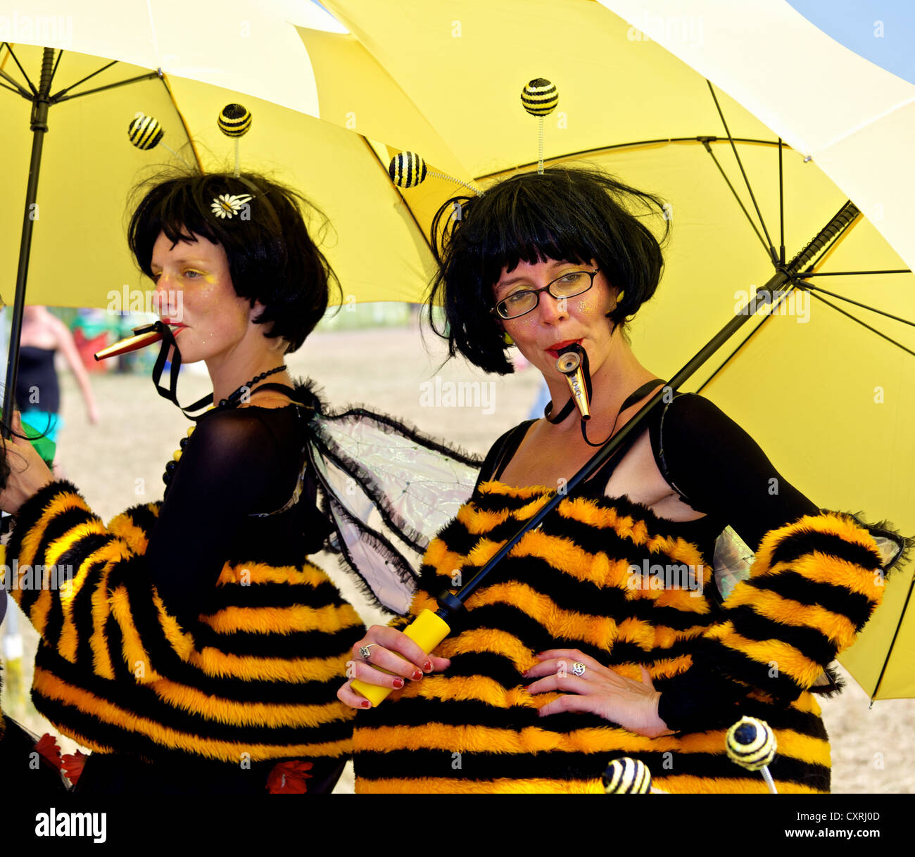 Due donne giocando Kazoos mentre riparo dal sole sotto un grande ombrello giallo presso il festival di Glastonbury Foto Stock