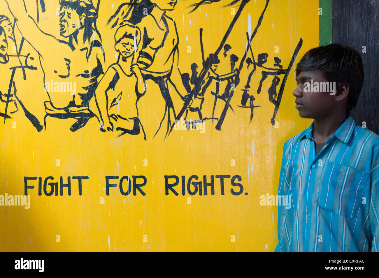 Il ragazzo, ex bambini operaio in piedi di fronte a slogan "lotta per i diritti dei cittadini' su un dipinto di giallo a parete, Kutties Rajiyam, il mondo dei piccoli Foto Stock
