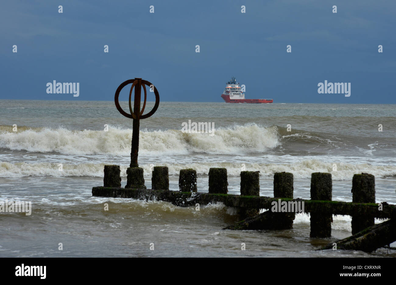 Maltempo con oceaniche nave per la fornitura di piattaforme petrolifere e tempestoso mare colpendo pennelli in spiaggia, Aberdeen, Regno Unito Foto Stock