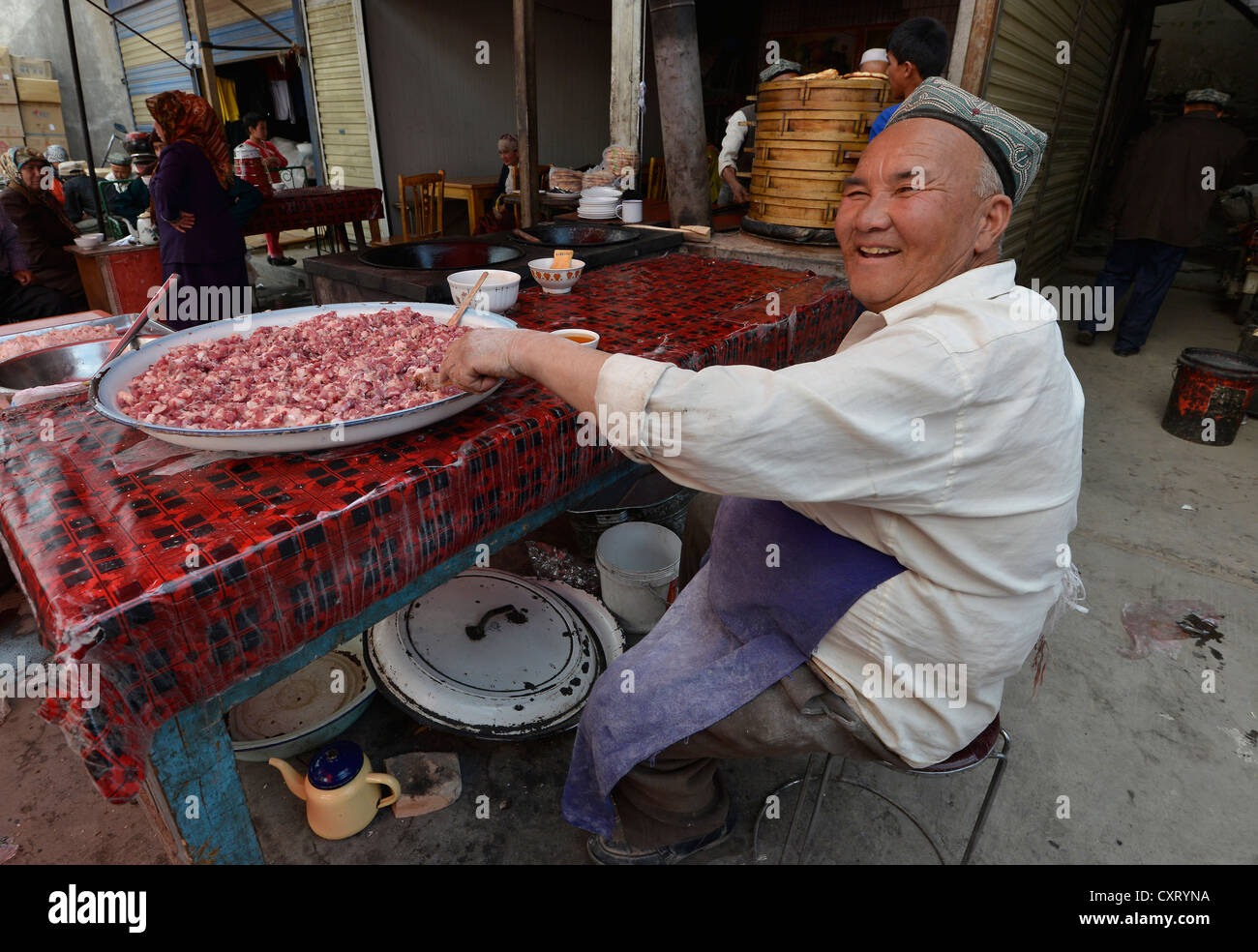 Mercato di domenica, anziani Uyghur uomo con un tradizionale hat vendita di carne di montone tritata, Musulmana bazaar, Uighur, Kashgar, Xinjiang, Cina Foto Stock