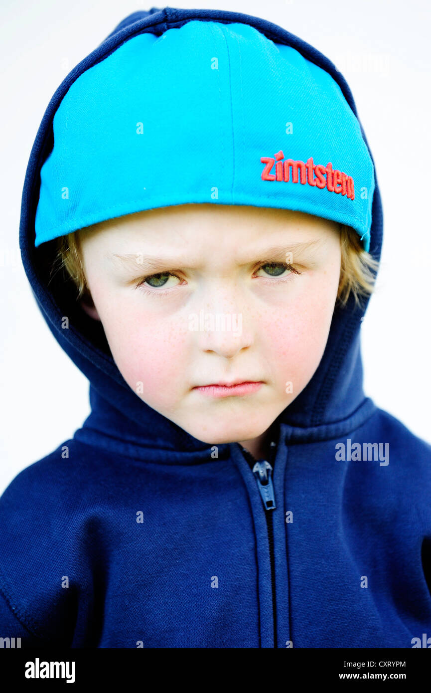 Grim di fronte 5-anno-vecchio ragazzo che indossa un cappello da baseball e una giacca felpa con cappuccio, ritratto Foto Stock