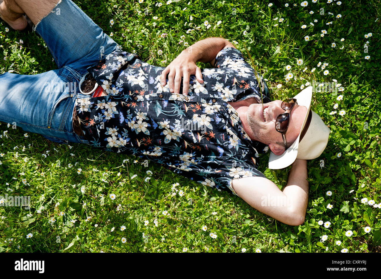 Uomo sorridente indossando un cappello di paglia, occhiali da sole e una  camicia hawaiana, giacente in un prato fiorito, ha una lama di erba in  bocca Foto stock - Alamy