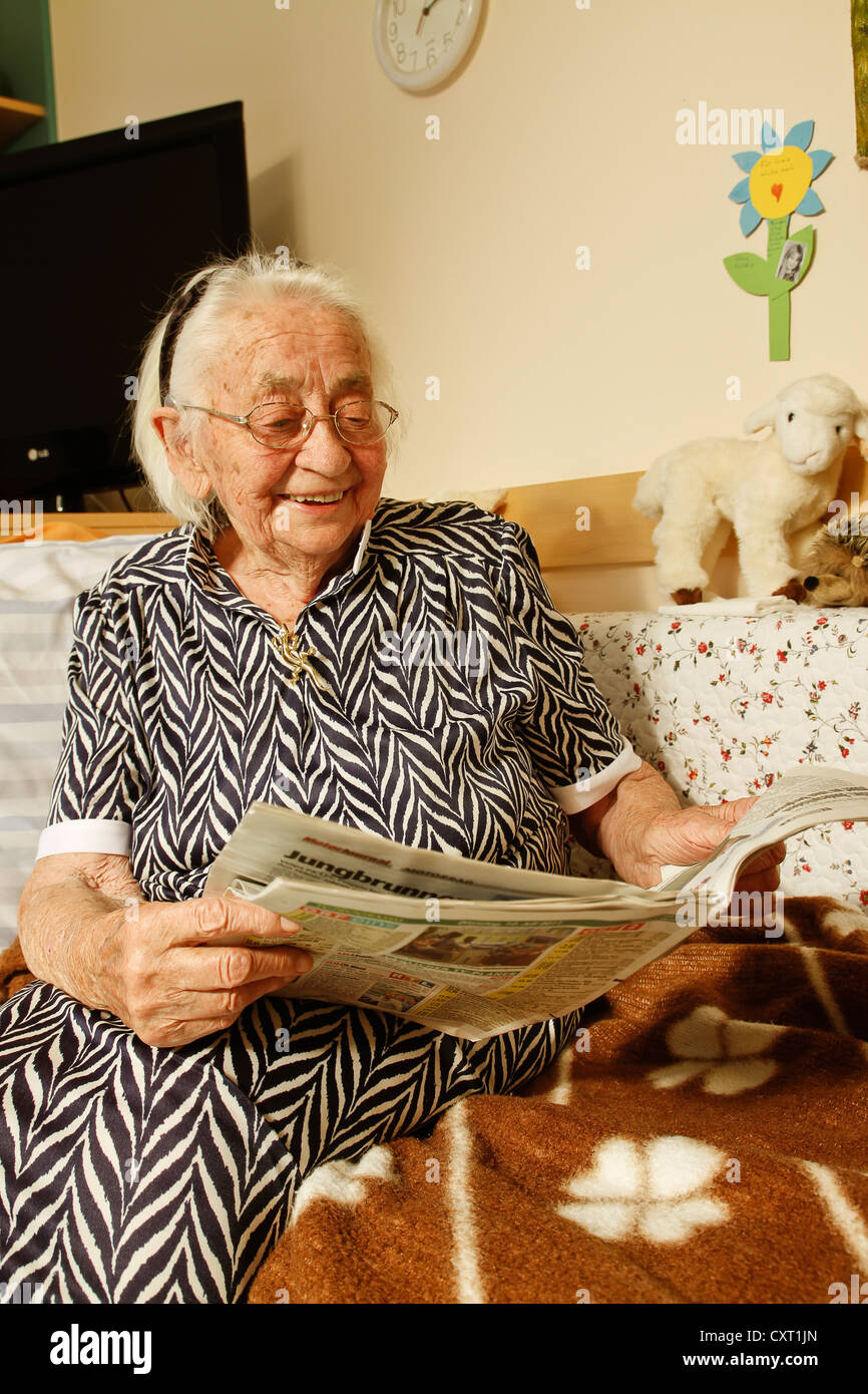 Donna anziana leggendo un giornale in una casa di cura Foto Stock