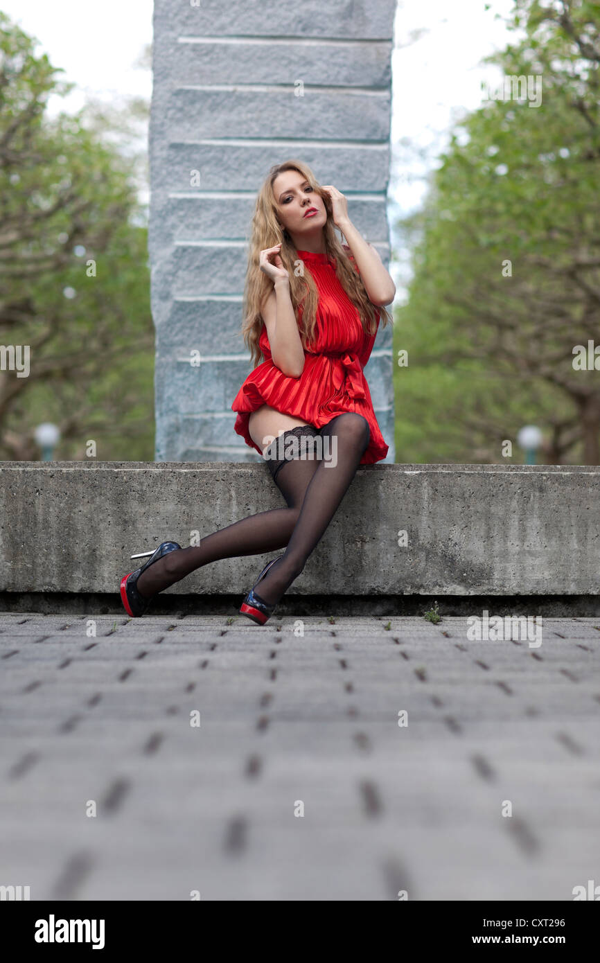 Giovane donna in un corto abito rosso, nero calze e tacchi alti seduti ad  una fontana, in posa Foto stock - Alamy