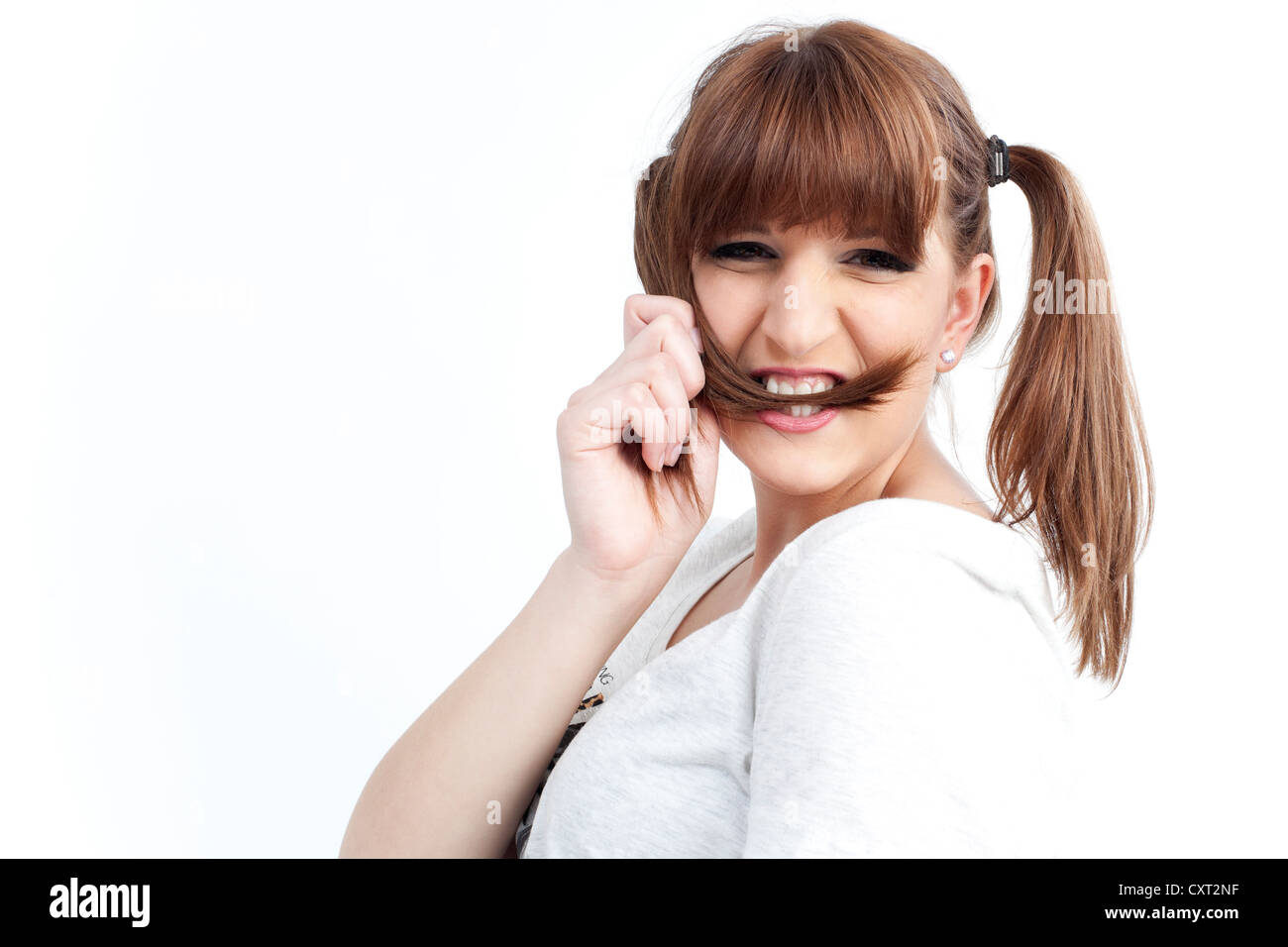 Giovane donna di mordere su una ciocca di capelli, sorridente Foto Stock