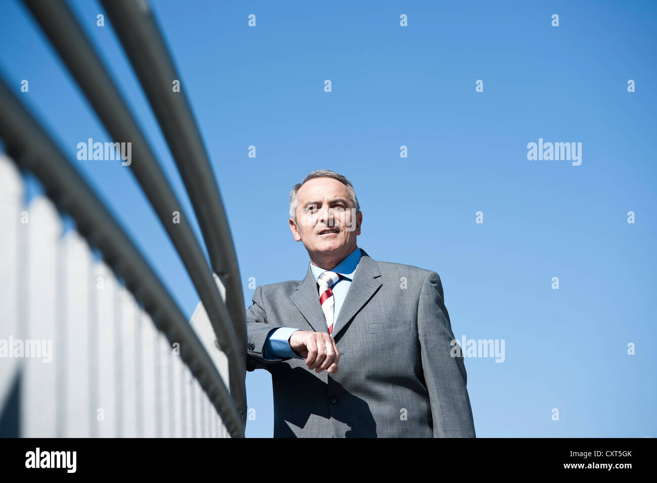 Imprenditore in piedi ad una ringhiera e guardando in lontananza Foto Stock