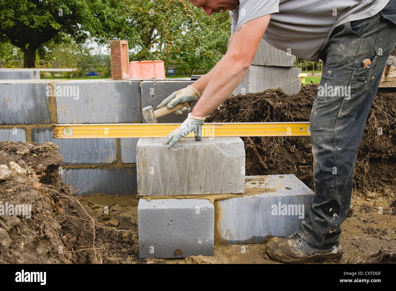 Muratore utilizzando un martello forfettaria a livello di blocco di calcestruzzo durante la costruzione di muro di fondazione Foto Stock
