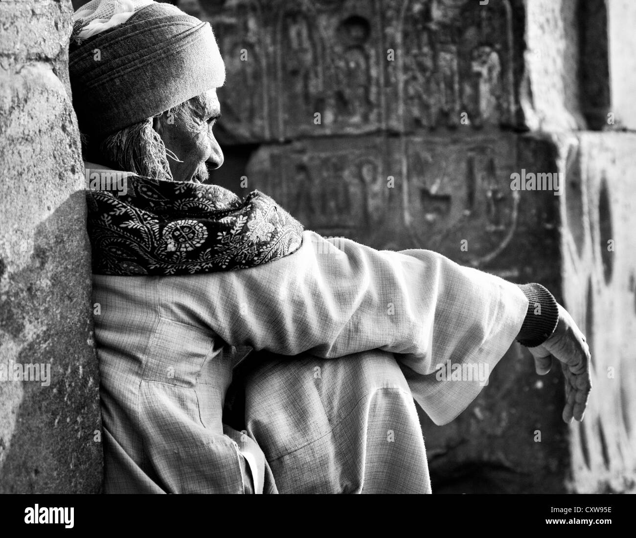 Egyptian uomo seduto nel sole di mezzogiorno indossando il tradizionale abbigliamento egiziano. Foto Stock