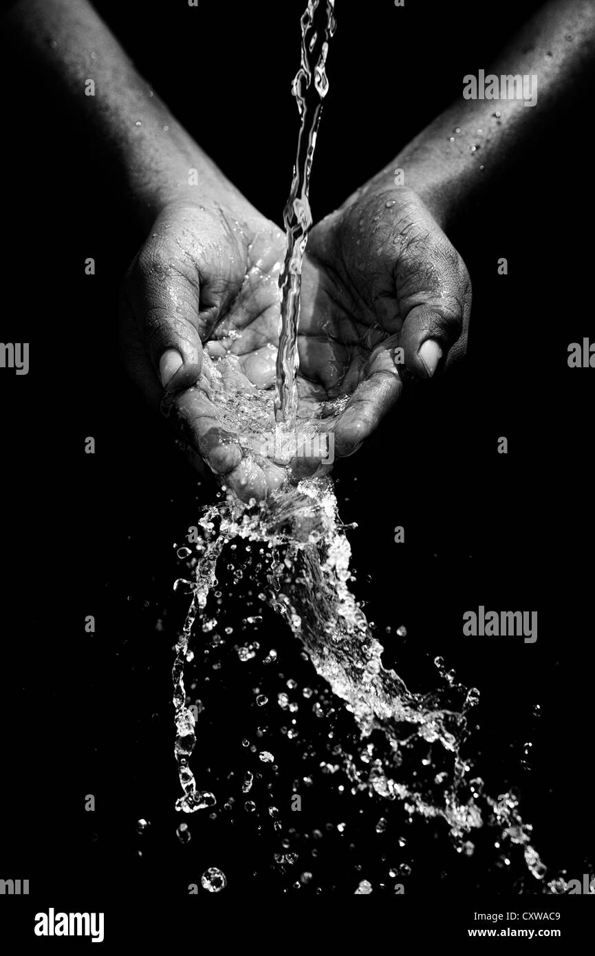 Indian mans mani a tazza la cattura di acqua versata su sfondo nero. Monocromatico Foto Stock