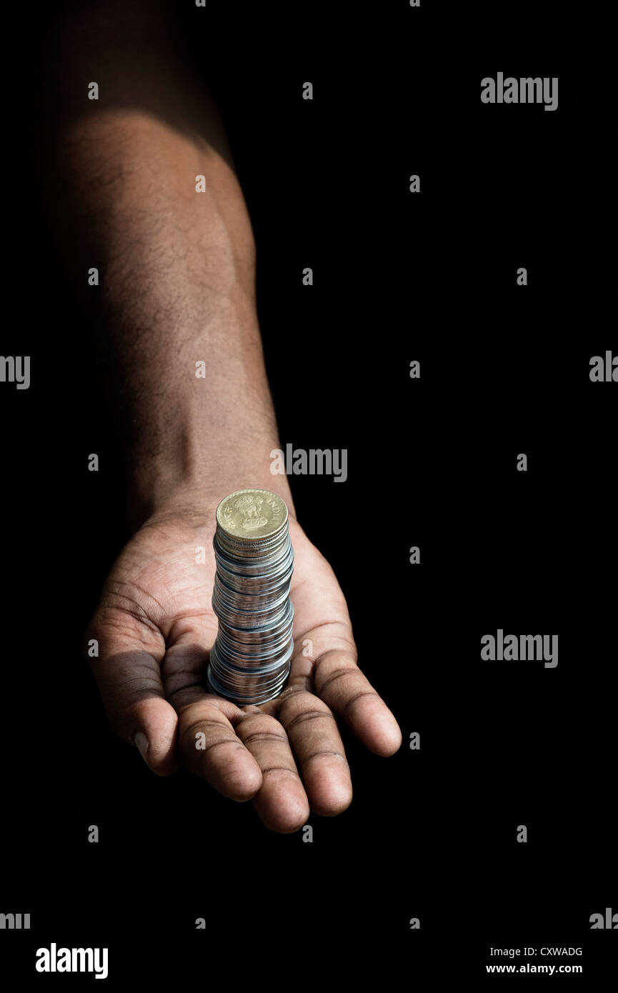 Indian mans mano con una pila di monete in rupie contro uno sfondo nero Foto Stock