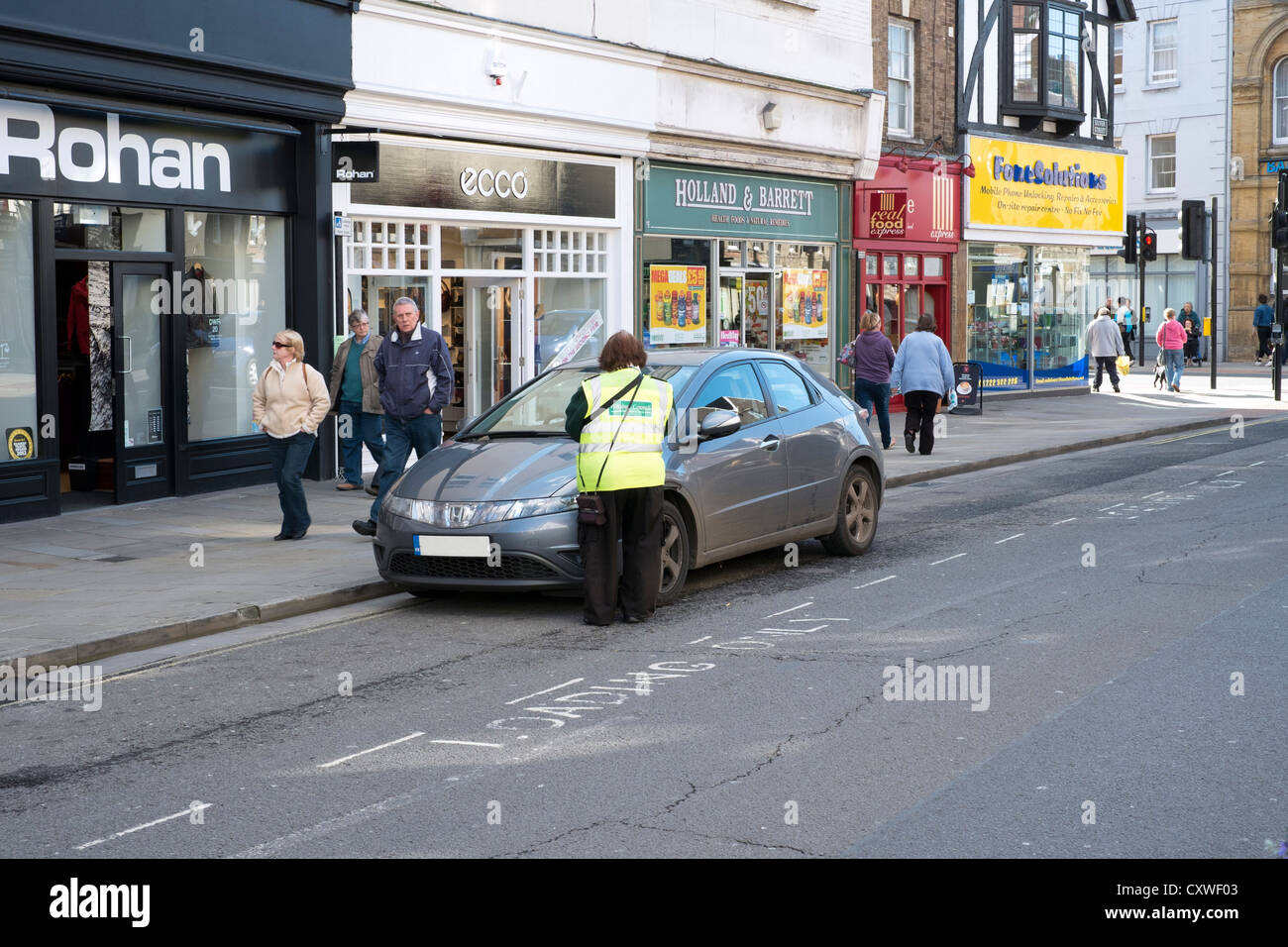 Il traffico del Regno Unito operaio o parcheggio Ambasciatore mettendo un biglietto di parcheggio su un illegalmente parcheggiato auto in strada Foto Stock
