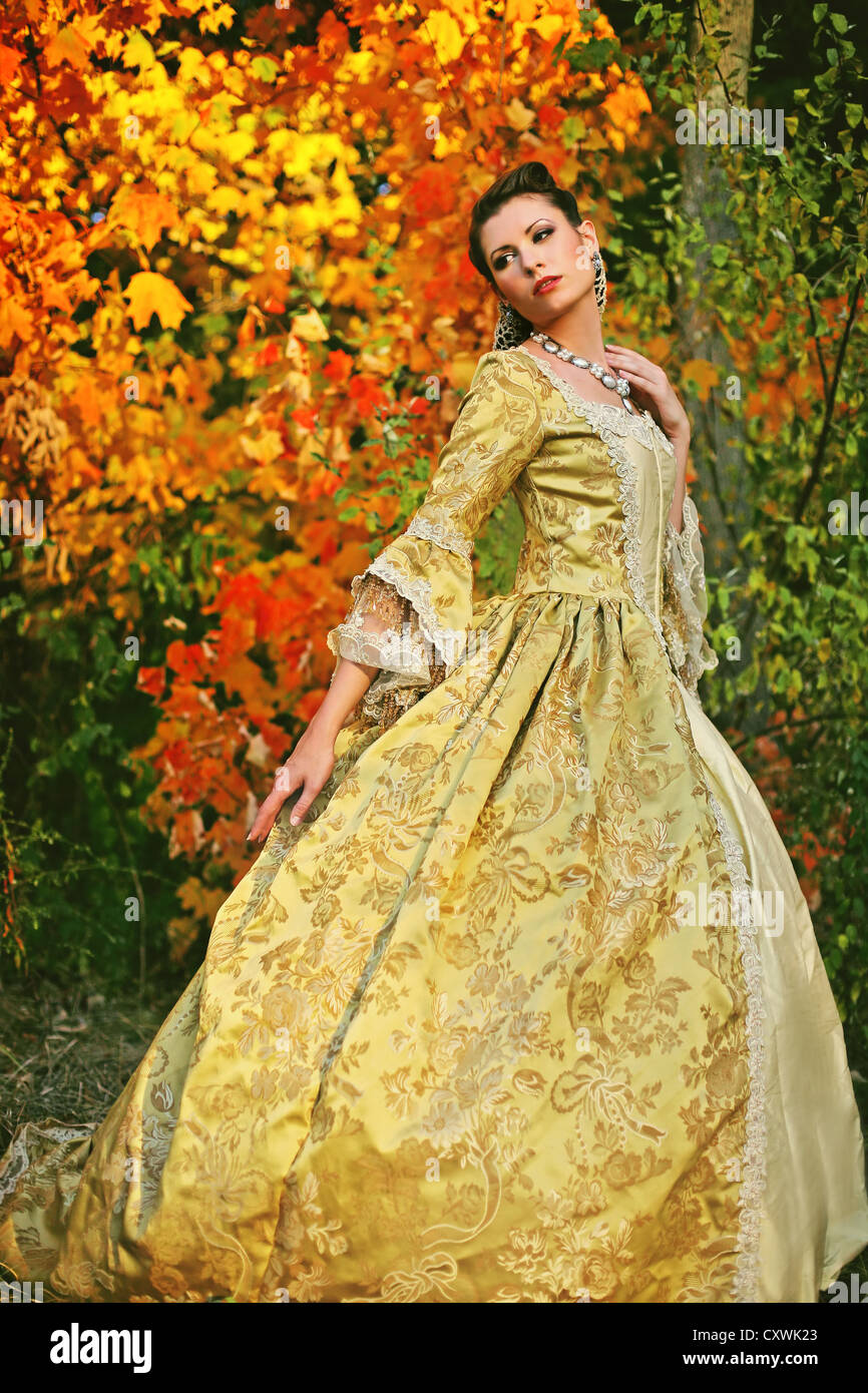 Una bella giovane donna nel suo tardo adolescenti o inizio 20s in un bellissimo abito di fantasia con colori d'autunno alberi Foto Stock
