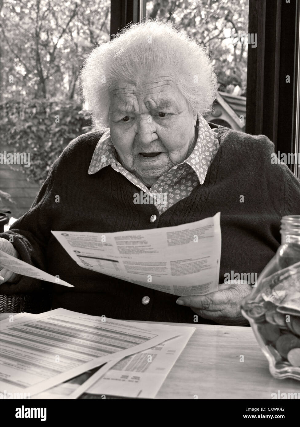 SPESE DI ENERGIA SHOCK SORPRESA preoccupato anziano anziano signora a casa lettura sua ultima energia / bollette casa investimenti lettere (B&W toned conversione) Foto Stock