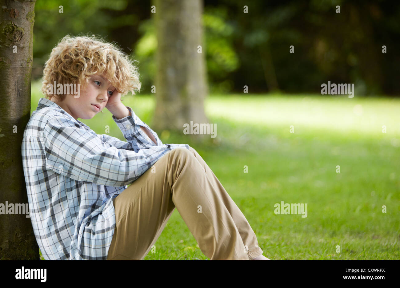 Triste cerca ragazzo appoggiata ad albero Foto Stock