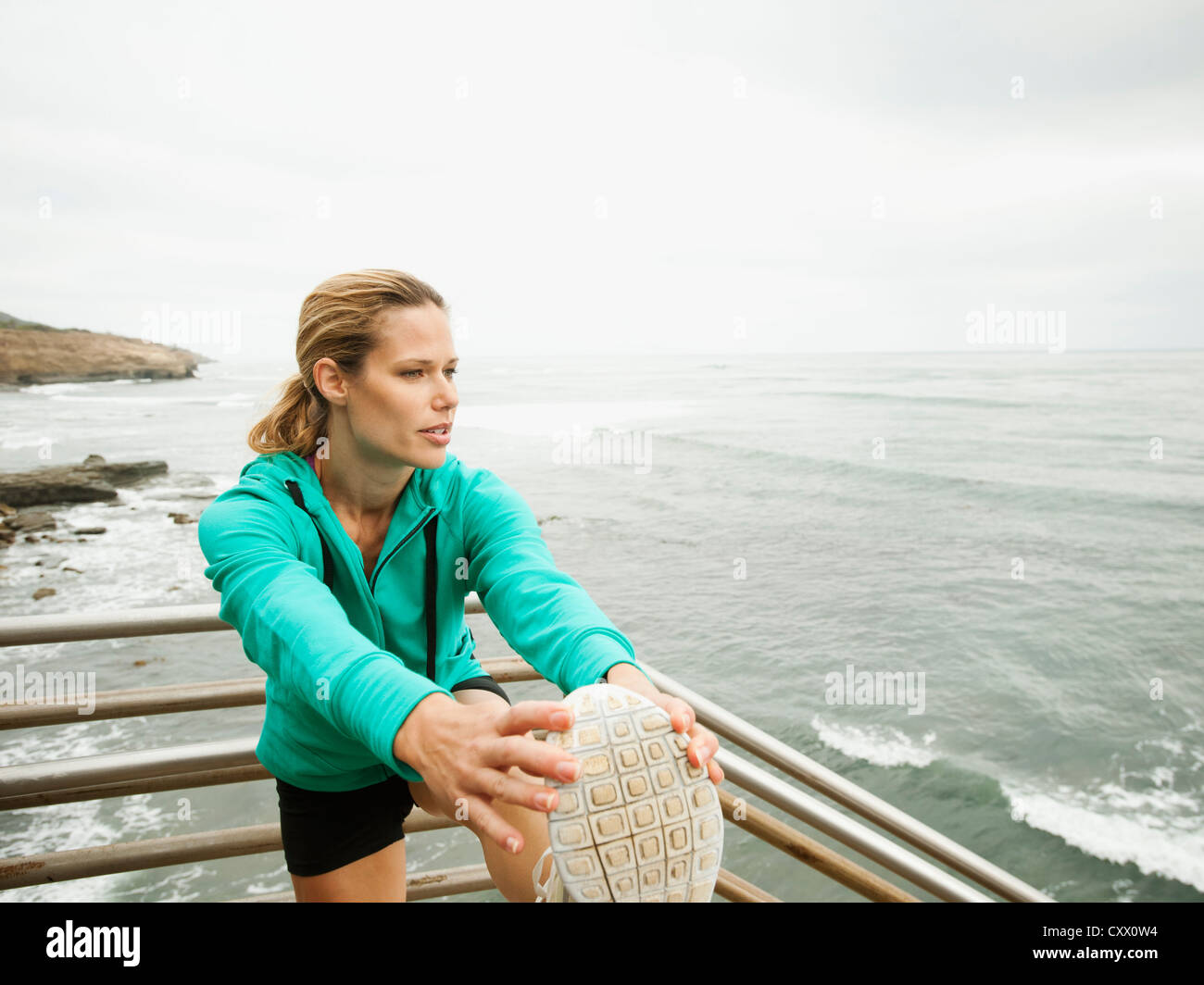 La donna caucasica stretching prima di esercitare accanto a Ocean Foto Stock