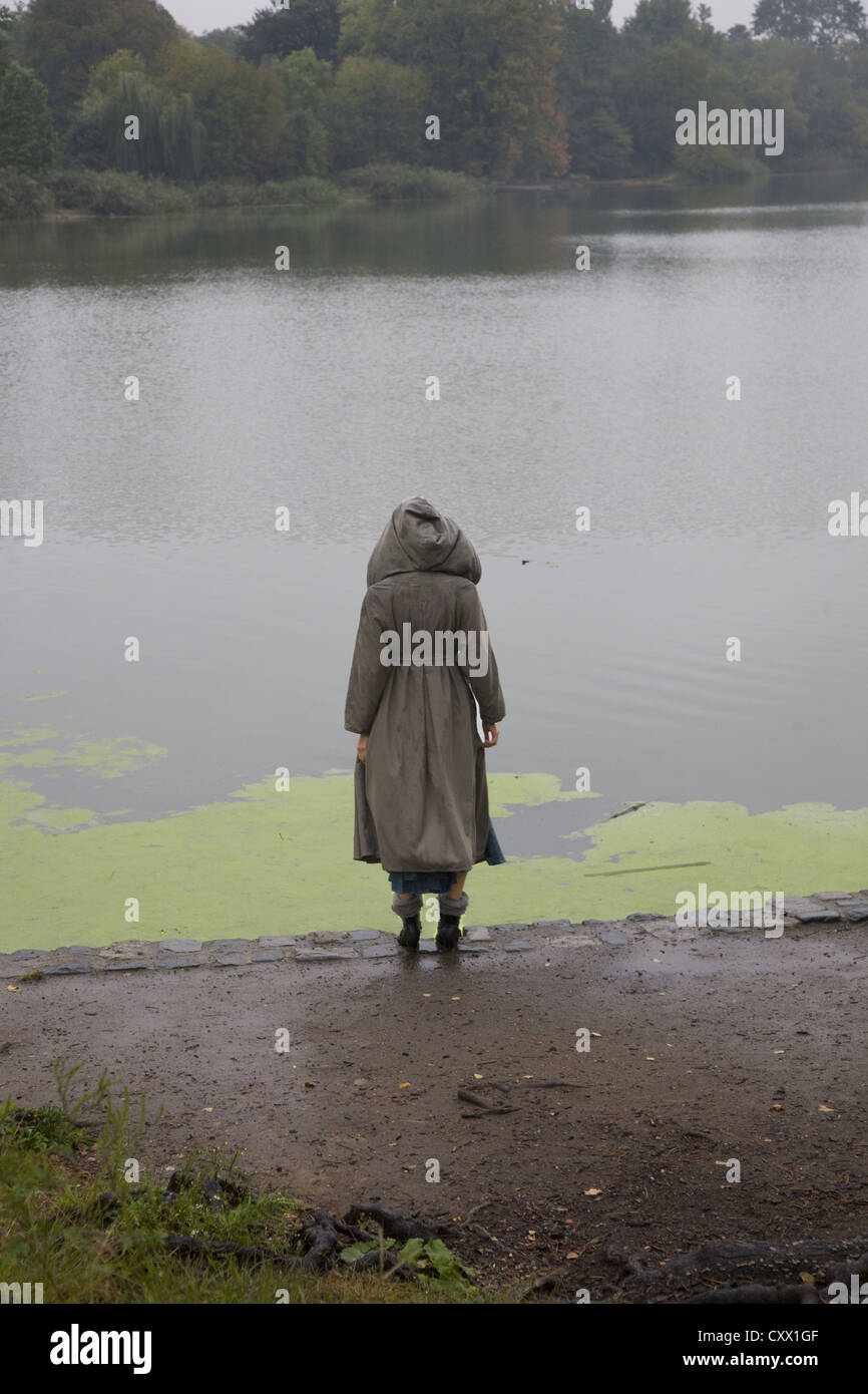 Giovane donna da sola in un giorno di pioggia lungo il lago in Prospect Park di Brooklyn, New York. Foto Stock