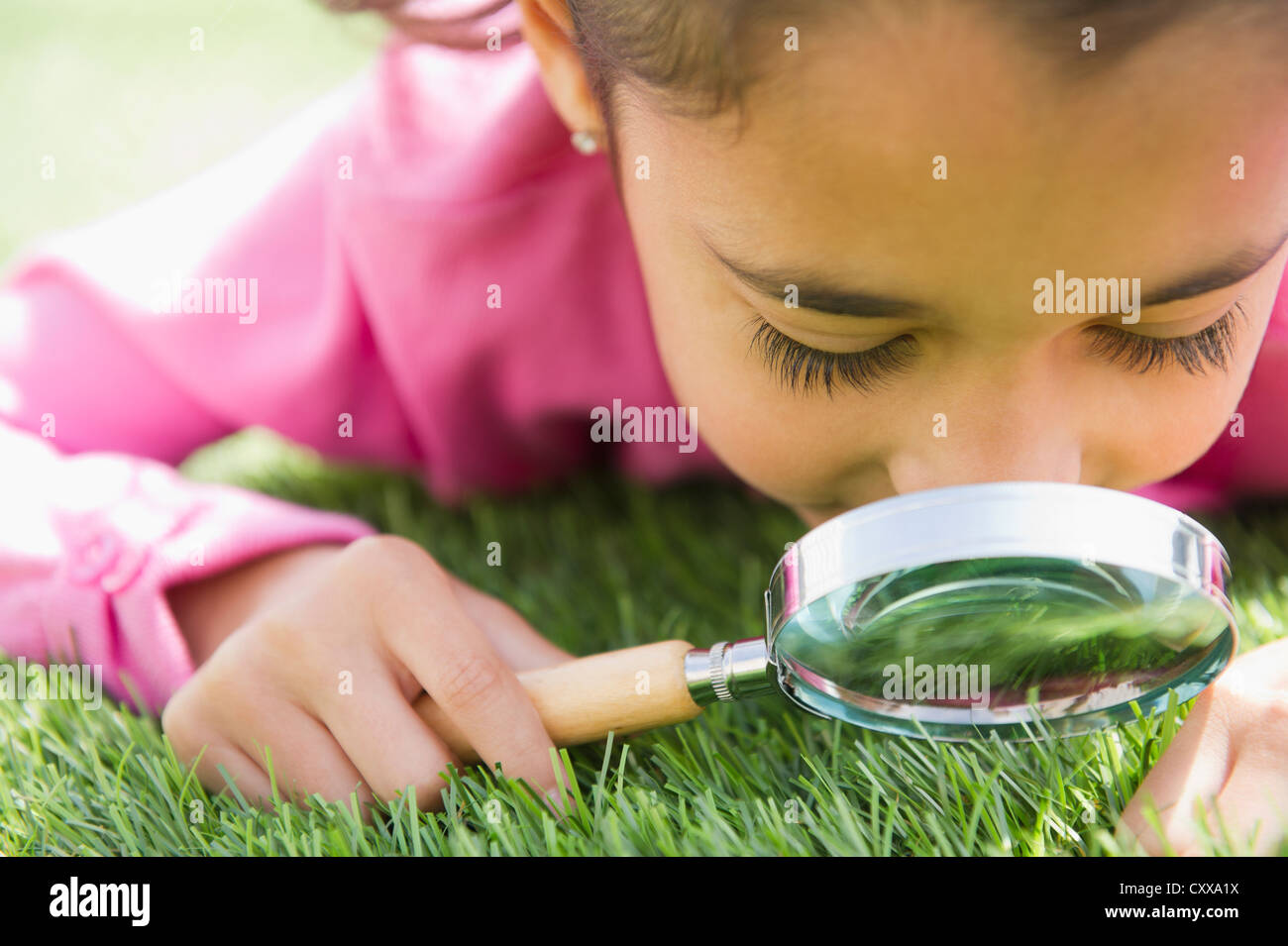 Razza mista ragazza guardando l'erba con lente di ingrandimento Foto Stock
