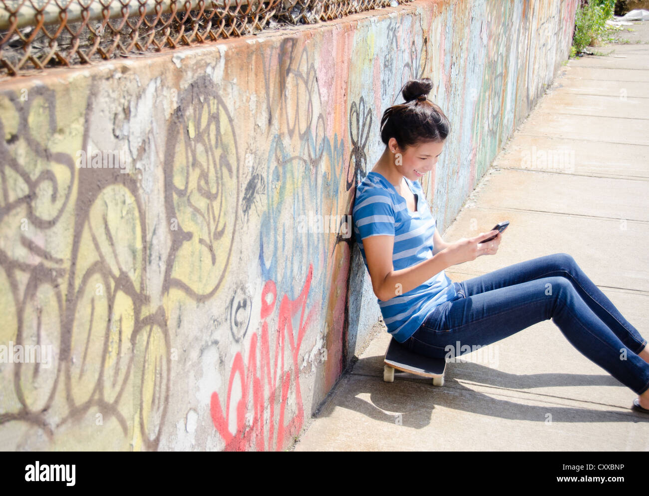 Asian donna seduta su skateboard tramite telefono cellulare Foto Stock