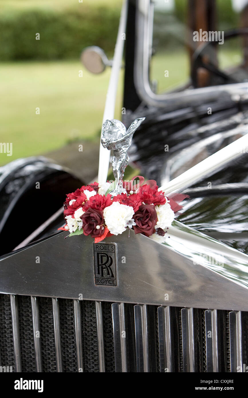 Rolls Royce classic vintage dettaglio auto che mostra una parte della griglia anteriore, badge e spirito di ecstasy statua d'argento inanellati da fiori Foto Stock