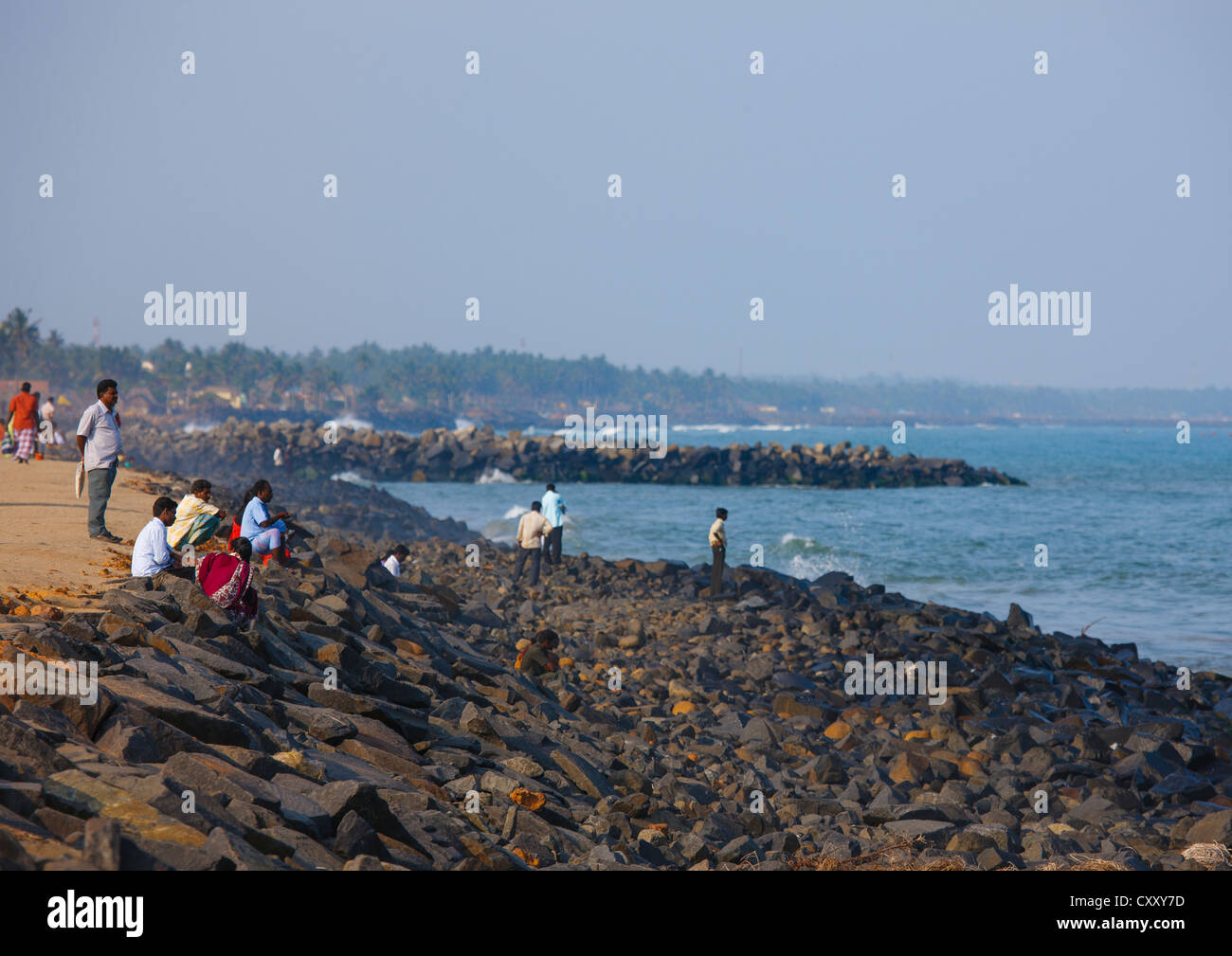 La gente seduta sulle rocce di una Seawall a Pondicherry Lungomare cercando Toowards l'orizzonte, India Foto Stock