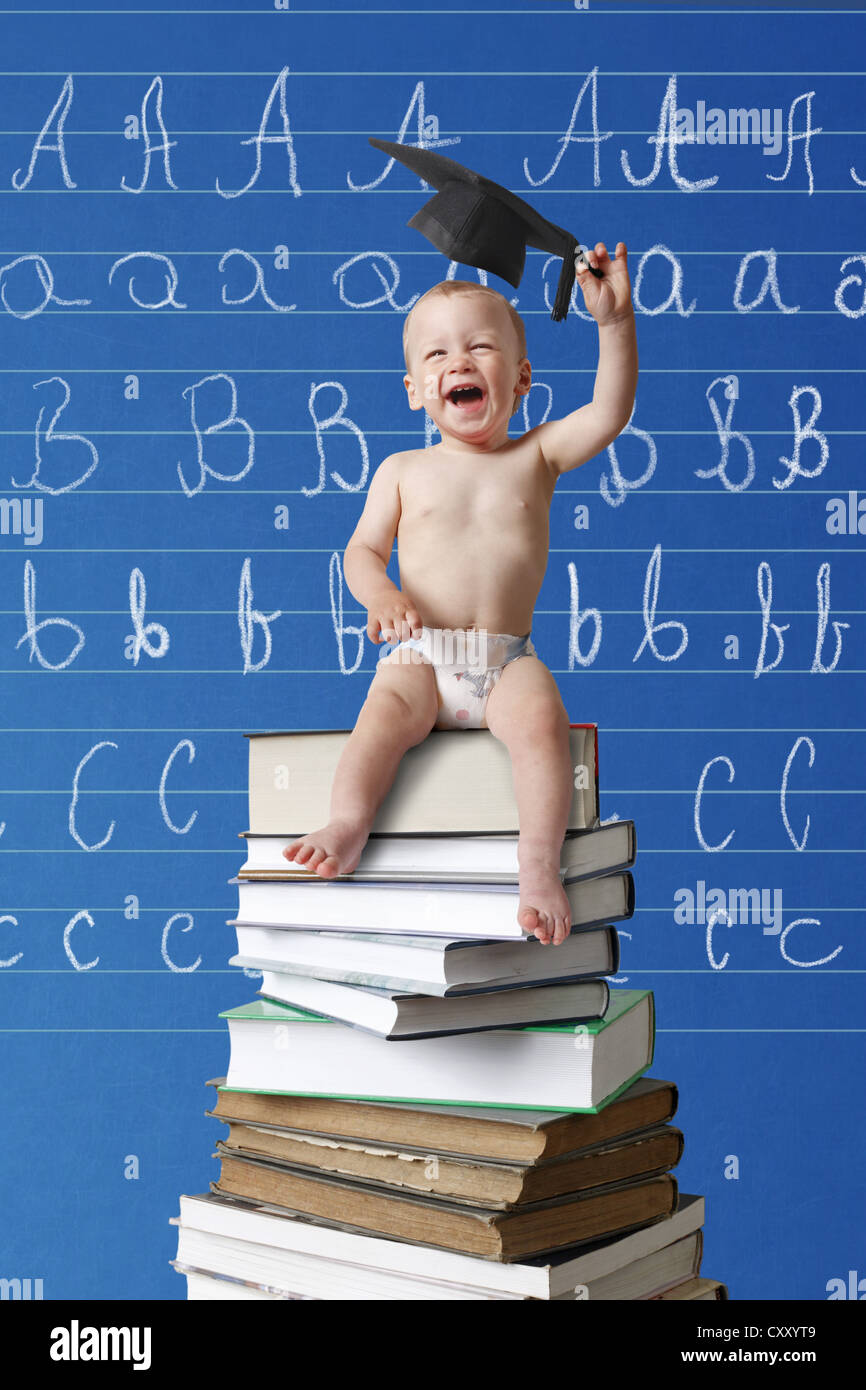 Ridendo di neonati tenendo un cappuccio di graduazione seduto su una pila di libri di fronte a una scuola lavagna con l ABC Foto Stock